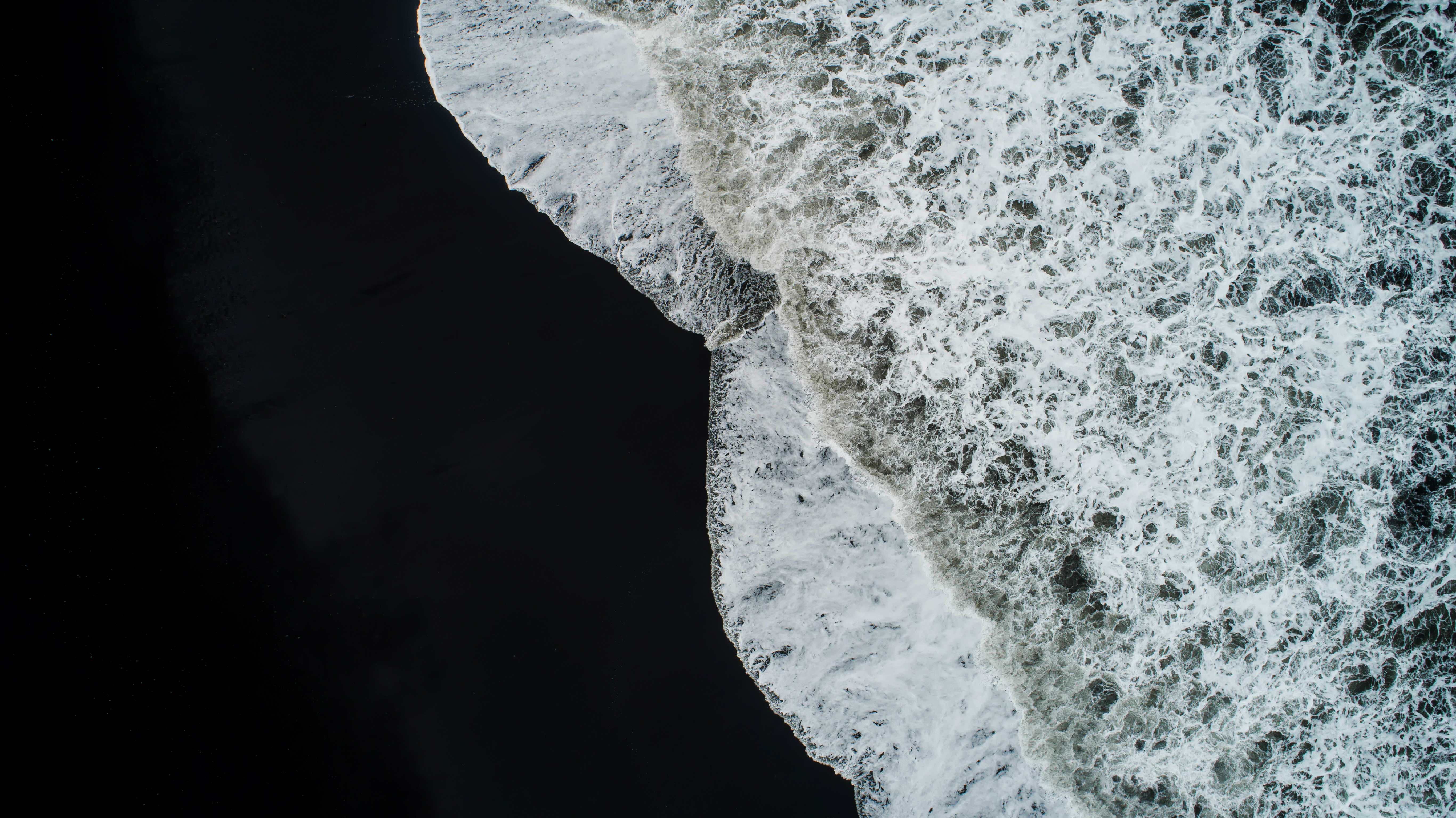 en svart strand med vitt vågskvalp